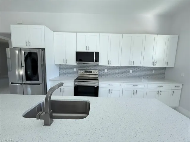 Kitchen featuring appliances with stainless steel finishes, backsplash, white cabinetry, and light stone counters
