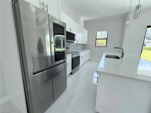 Kitchen featuring appliances with stainless steel finishes, white cabinets, light stone countertops, and backsplash