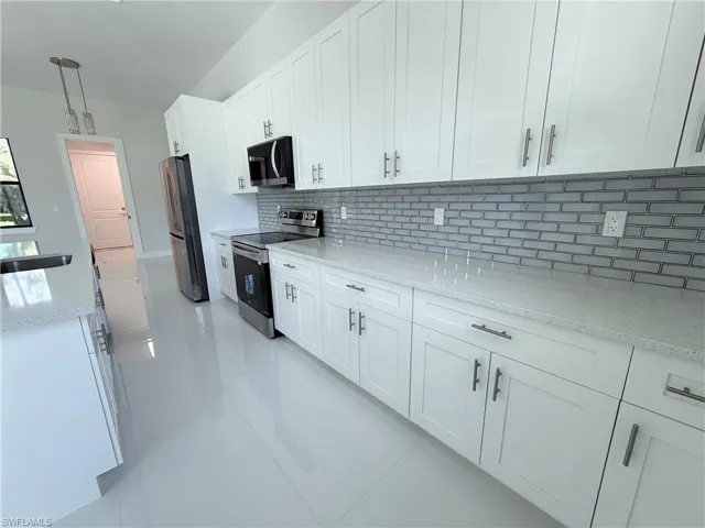 Kitchen with white cabinetry, light stone counters, stainless steel appliances, and decorative light fixtures