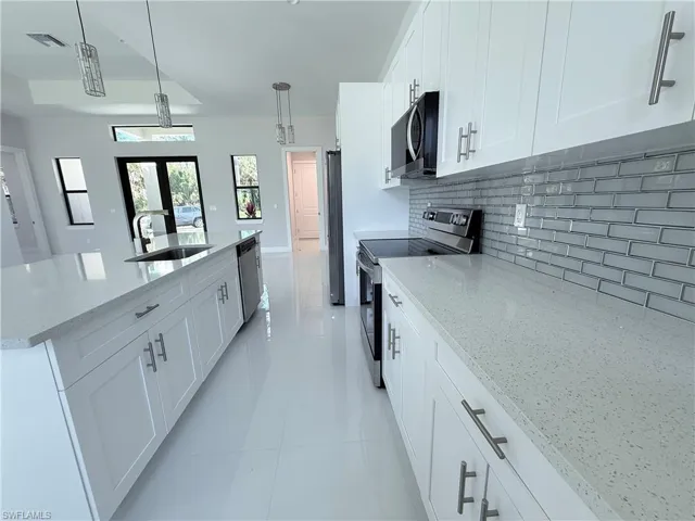 Kitchen featuring appliances with stainless steel finishes, white cabinets, light stone counters, a center island with sink, and hanging light fixtures
