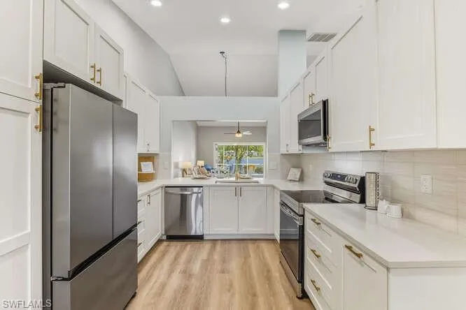 Newly updated Kitchen with stainless steel appliances, white cabinetry, tile backsplash, hanging light fixtures, and lofted ceiling.