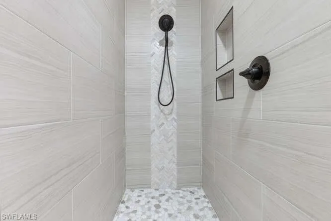 Newly updated primary bath walk-in shower with a mix of decorative ceramic tile, built-in accessory holder and zero transition entry into bath area.