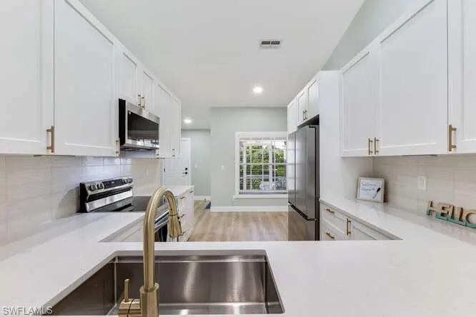 Newly updated Kitchen with stainless steel appliances, white cabinetry, tile backsplash, hanging light fixtures, and lofted ceiling.