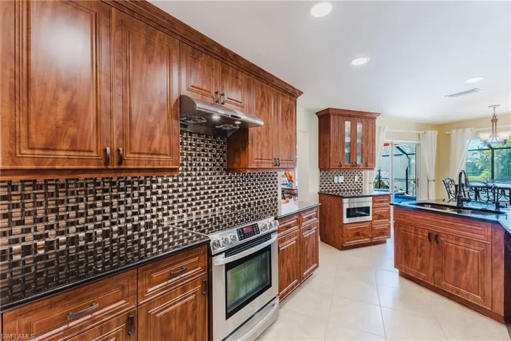 Kitchen featuring tasteful backsplash, appliances with stainless steel finishes, brown cabinets, under cabinet range hood, and recessed lighting
