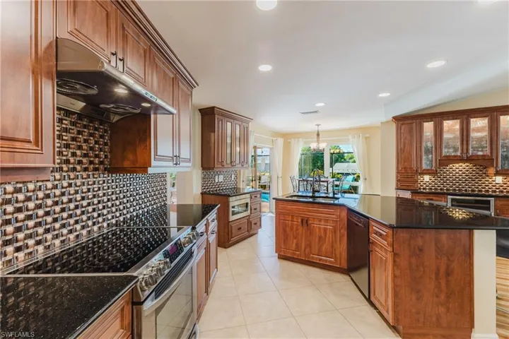 Kitchen featuring decorative backsplash, glass insert cabinets, appliances with stainless steel finishes, under cabinet range hood, and dark stone countertops