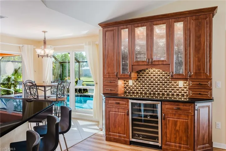 Bar area featuring decorative light fixtures, wine cooler, backsplash, and dark stone counters