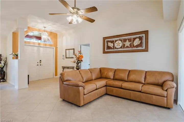 Living room with light tile patterned floors, high vaulted ceiling, ceiling fan, and a chandelier