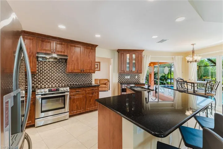 Kitchen featuring stainless steel appliances, dark stone counters, backsplash, brown cabinetry, and hanging light fixtures