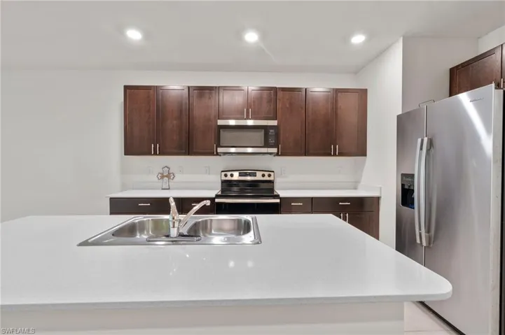 Kitchen with appliances with stainless steel finishes, dark brown cabinetry, light stone counters, and recessed lighting