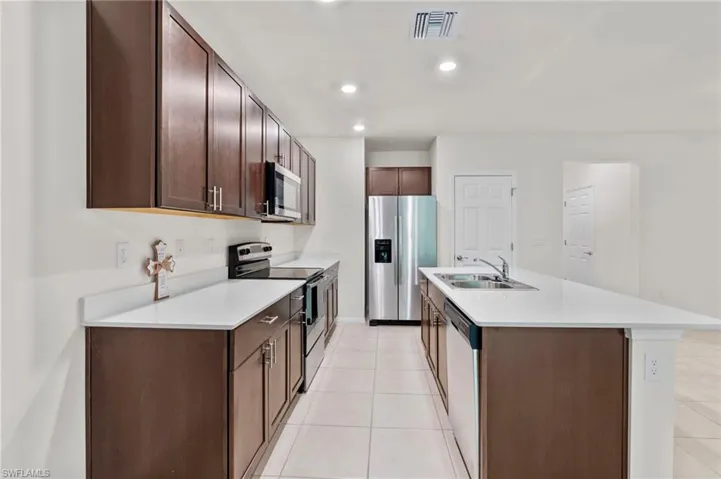 Kitchen featuring appliances with stainless steel finishes, dark brown cabinets, light tile patterned floors, recessed lighting, and a kitchen island with sink