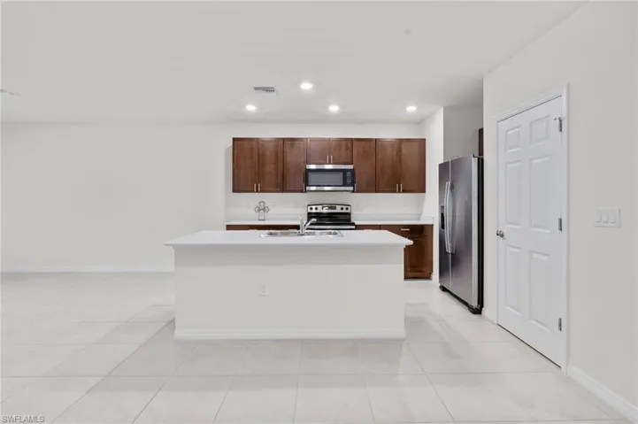Kitchen featuring stainless steel appliances, a kitchen island with sink, dark brown cabinets, light tile patterned floors, and recessed lighting