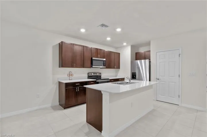 Kitchen featuring stainless steel appliances, light countertops, a kitchen island with sink, dark brown cabinets, and light tile patterned floors