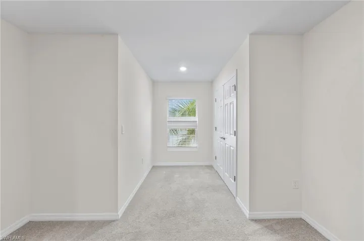 Hallway with light colored carpet and baseboards