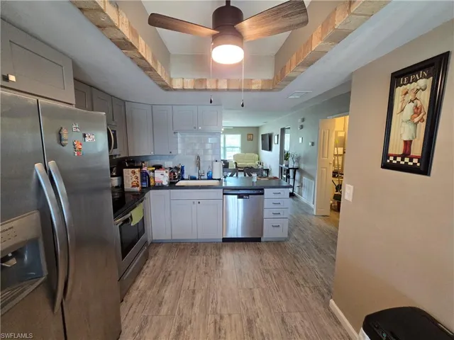 Kitchen featuring wood-finish flooring, stainless steel appliances, light gray cabinetry, and dark countertops