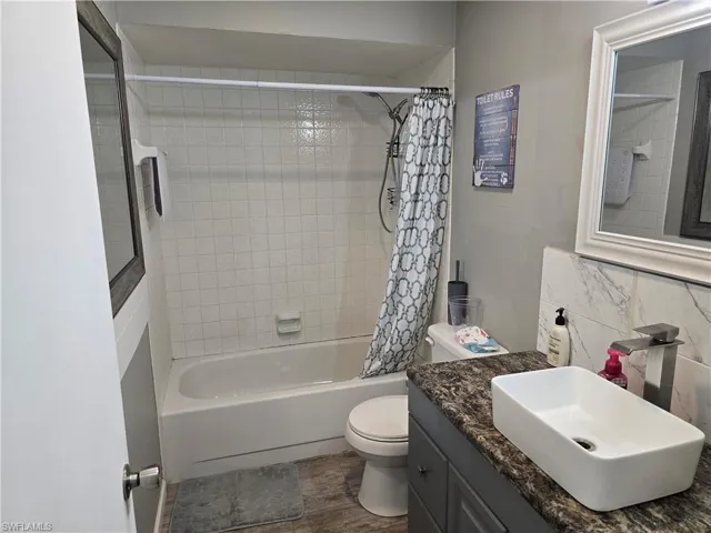 Bathroom featuring a tiled shower/tub combination, pedestal toilet, a vanity with a vessel sink, and a framed mirror