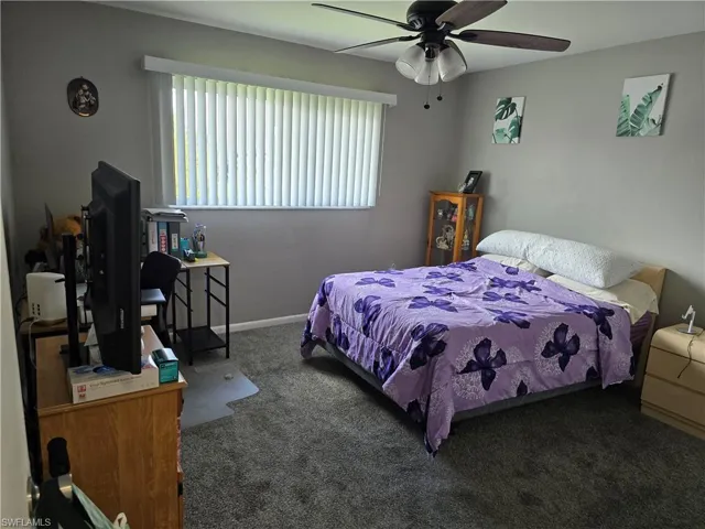 Plush carpeted flooring, window with vertical blinds, ceiling fan with integrated lighting, and neutral wall tones