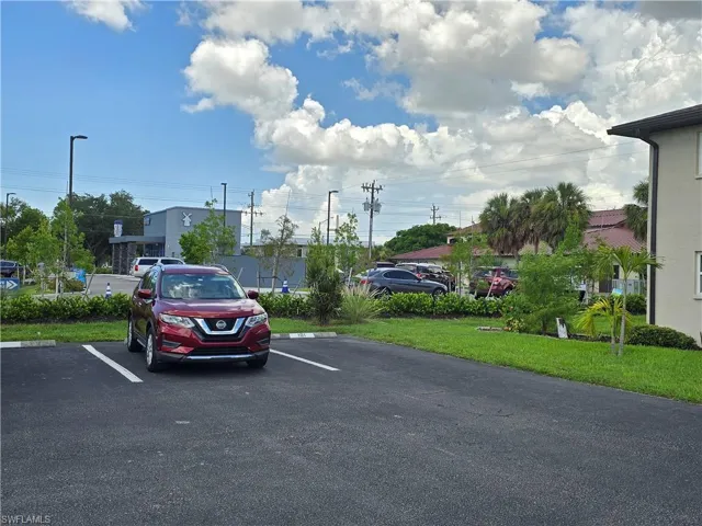Paved parking lot with designated spaces, bordered by landscaped areas featuring grass and various plantings