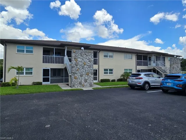 Two-story building exterior with stone veneer accents, multiple screened-in patios, and a well-maintained asphalt parking area