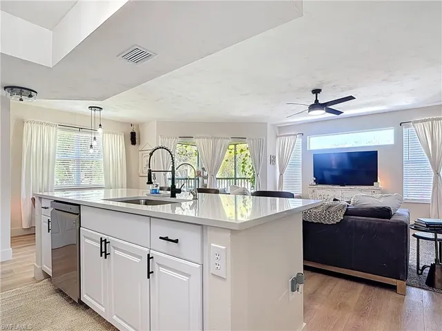 Kitchen with light wood-type flooring, an island with sink, a sink, and visible vents