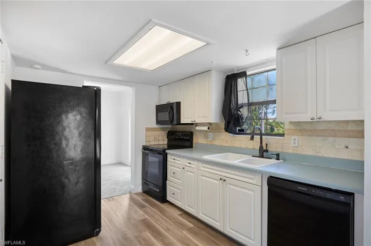 Kitchen featuring black appliances, a sink, white cabinets, and light wood-style floors