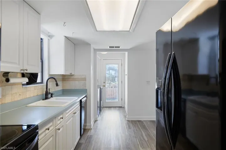 Kitchen with a sink, light wood-style floors, tasteful backsplash, white cabinetry, and black fridge