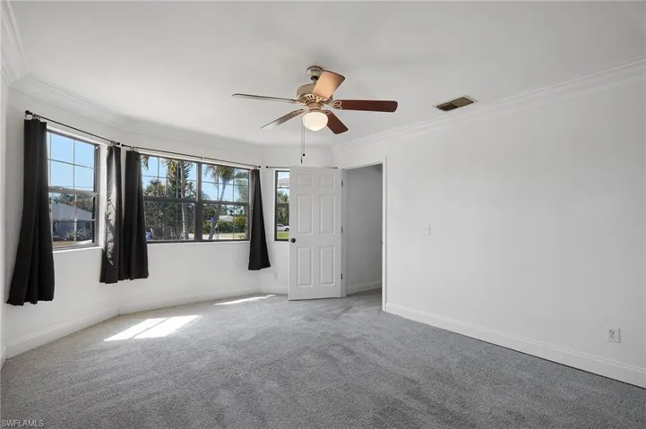 Carpeted spare room featuring a ceiling fan, baseboards, crown molding, and visible vents