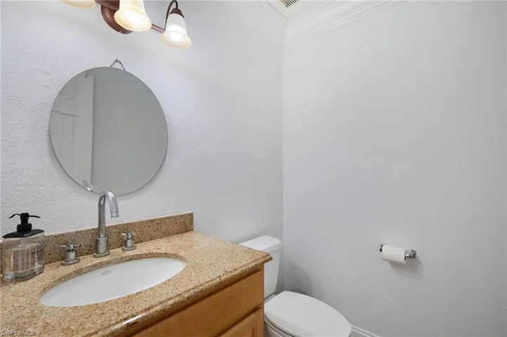 Half bathroom featuring crown molding, toilet, and vanity