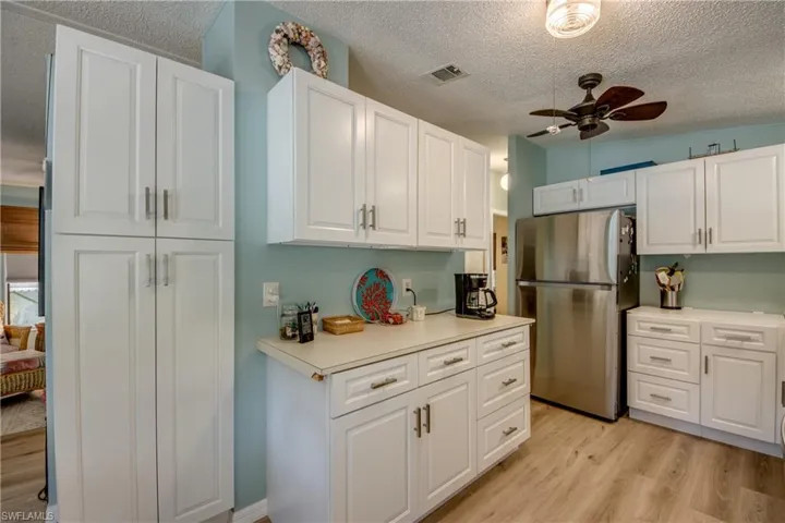 There is a new counter top installed. Kitchen featuring a ceiling fan, freestanding refrigerator, light wood-type flooring, light countertops, and white cabinets
