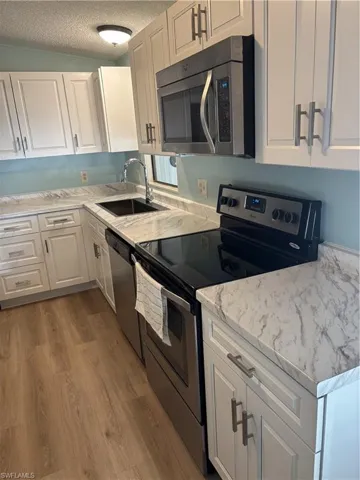 Kitchen featuring white shaker-style cabinetry, a stainless steel over-the-range microwave, a stainless steel electric range, a stainless steel dishwasher, and wood-finish flooring