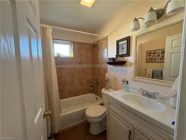 Bathroom with shower / bathtub combination with curtain, vanity, and dark tile patterned floors