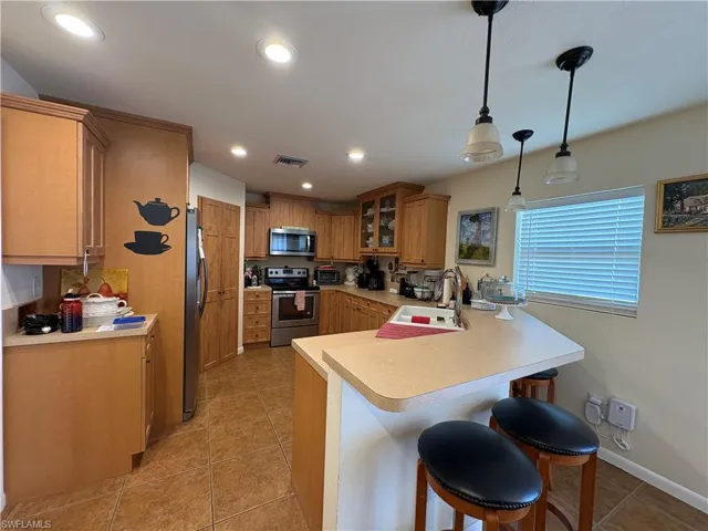 Kitchen featuring appliances with stainless steel finishes, light countertops, a breakfast bar area, pendant lighting, and light tile patterned floors