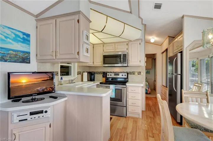 Kitchen with lofted ceiling, light wood-type flooring, stainless steel appliances, kitchen peninsula, and crown molding