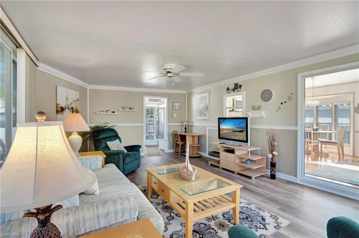 Living room with ceiling fan with notable chandelier, hardwood / wood-style flooring, and crown molding