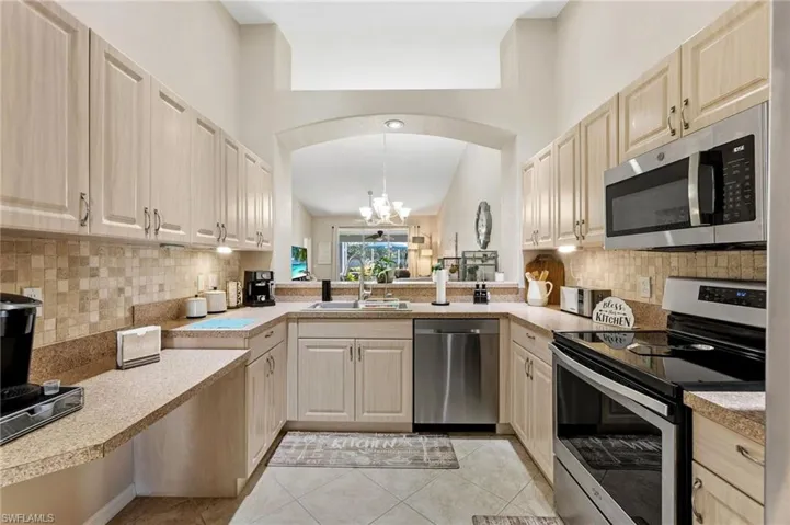 Kitchen featuring stainless steel appliances, a chandelier, pendant lighting, light tile patterned flooring, and light countertops