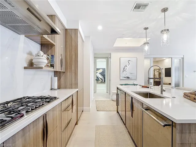 Kitchen featuring light wood-type flooring, dishwasher, pendant lighting, wall chimney exhaust hood, and sink