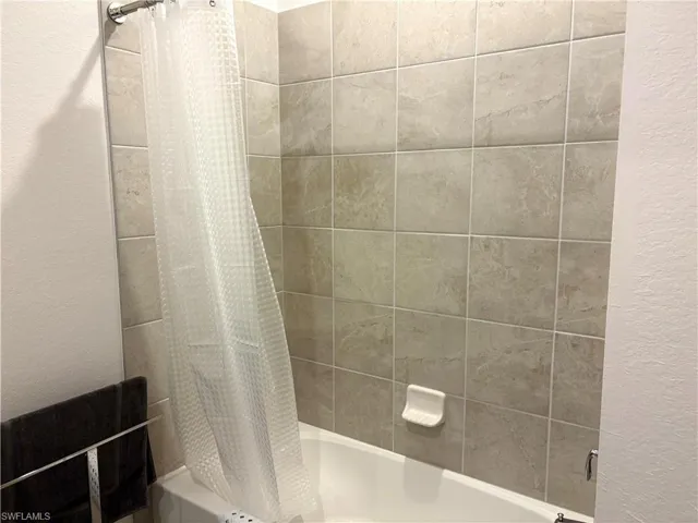 Bathroom featuring shower / tub combo with curtain and a textured wall
