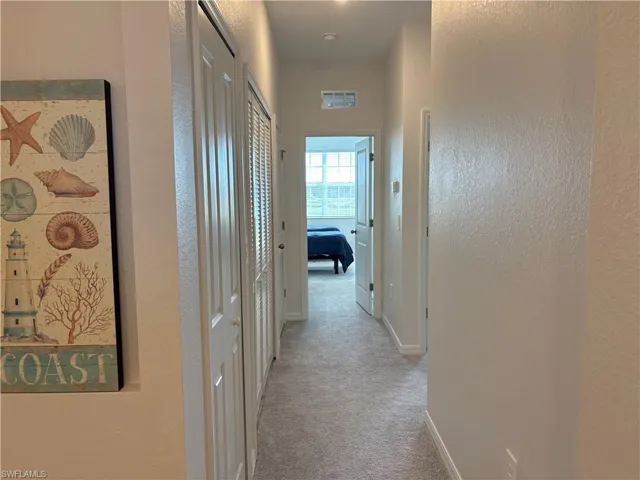 Corridor featuring a textured wall and light carpet