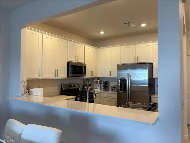 Kitchen featuring white cabinetry, stainless steel appliances, light stone counters, recessed lighting, and a peninsula