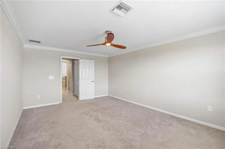 Carpeted empty room featuring ceiling fan and ornamental molding