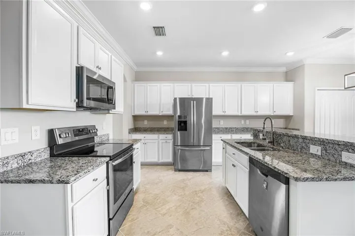 Kitchen with appliances with stainless steel finishes, ornamental molding, sink, dark stone countertops, and white cabinets