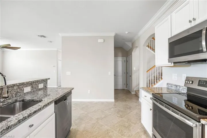 Kitchen featuring appliances with stainless steel finishes, light stone counters, white cabinetry, and ceiling fan