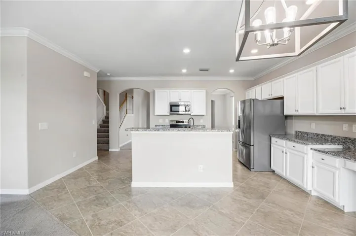 Kitchen featuring hanging light fixtures, an inviting chandelier, appliances with stainless steel finishes, white cabinetry, and ornamental molding