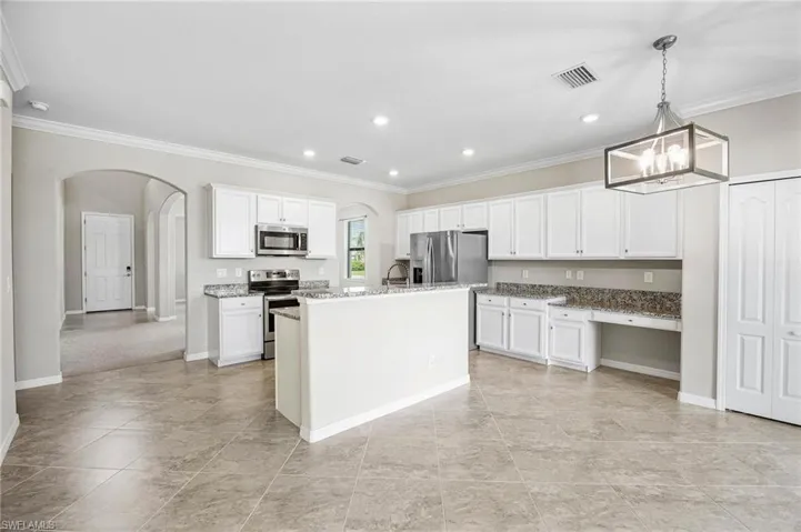 Kitchen featuring a center island with sink, pendant lighting, stainless steel appliances, ornamental molding, and white cabinetry