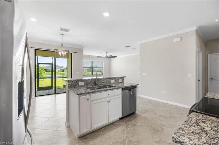 Kitchen featuring white cabinets, ceiling fan with notable chandelier, appliances with stainless steel finishes, sink, and an island with sink