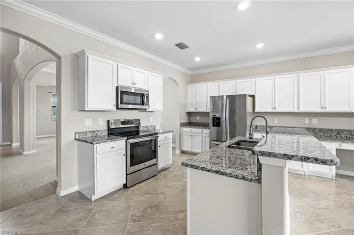 Kitchen featuring light carpet, crown molding, white cabinetry, stainless steel appliances, and sink