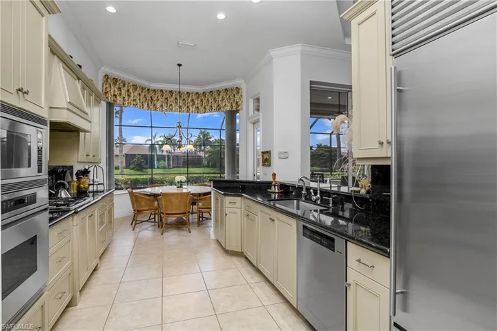 Kitchen with cream cabinets, built in appliances, hanging light fixtures, dark stone countertops, and sink