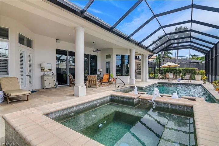 View of pool featuring glass enclosure, ceiling fan, pool water feature, a patio area, and an in ground hot tub