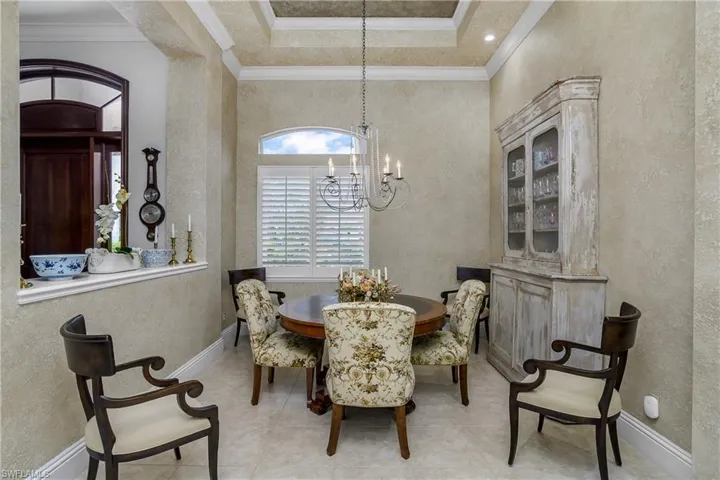 Dining space with an inviting chandelier, a healthy amount of sunlight, crown molding, and a raised ceiling