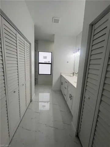 Full bath featuring a closet, double vanity, and light marble finish floors