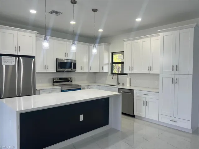 Kitchen featuring stainless steel appliances, light marble finish floors, pendant lighting, light stone countertops, and white cabinetry